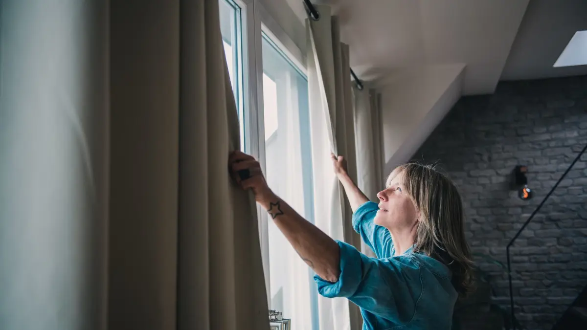 Eine Frau schliesst Vorhänge in einer Dachgeschosswohnung: ILLUSTRATION - Dachgeschosse werden bei sommerlichen Temperaturen schnell unangenehm heiß. (zu dpa: «Das hilft gegen Hitze (nicht nur) im Dachgeschoss») Foto: Zacharie Scheurer/dpa-mag - Honorarfrei nur für Bezieher des Dienstes dpa-Magazin +++ dpa-Magazin +++