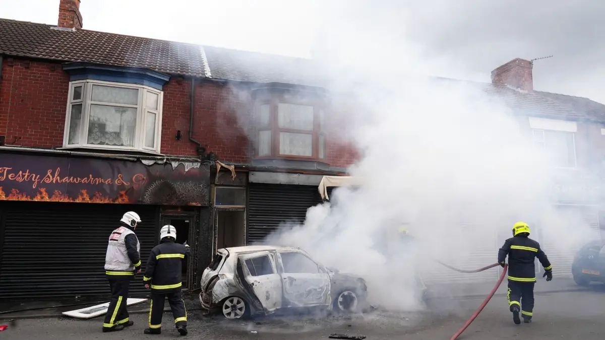 Ausschreitungen nach Messerangriff auf Kinder in Southport: 04.08.2024, Großbritannien, Middlesbrough: Feuerwehrleute löschen ein brennendes Auto in der Parliament Road in Middlesbrough während einer Anti-Einwanderungsdemonstration. Nach der Messerattacke auf Kinder in Southport am 29.07.2024 heizen zahlreiche nationalistische und antiislamische Proteste die Stimmung in Großbritannien auf. Foto: Owen Humphreys/PA Wire/dpa +++ dpa-Bildfunk +++