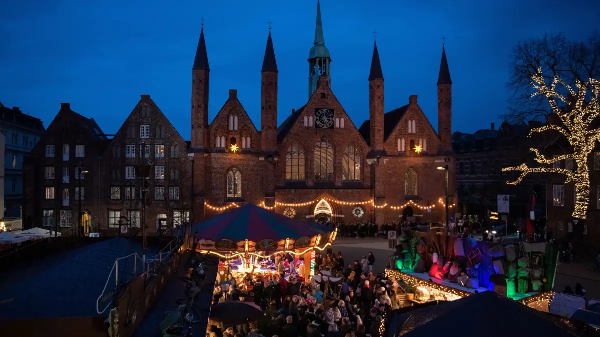 01.12.2018, Schleswig-Holstein, Lübeck: Menschen warten vor dem Eingang zum Kunsthandwerkermarkt im Heiligen-Geist-Hospital auf Einlass, während im Vordergrund auf einem Weihnachtsmarkt gefeiert wird. Der Kunsthandwerkermarkt in den Gemäuern aus dem 13. Jahrhundert hat bis zum 10. Dezember geöffnet. Foto: Rainer Jensen/dpa +++ dpa-Bildfunk +++