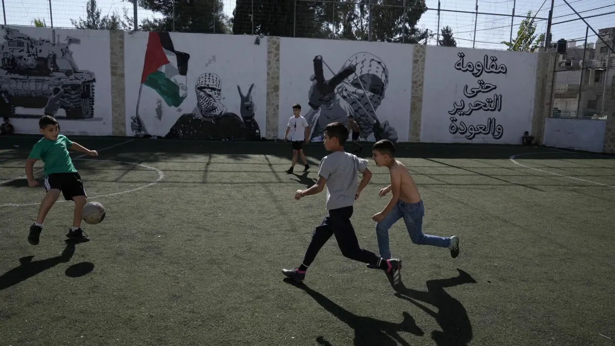 Nahostkonflikt -: 23.11.2024, Palästinensische Gebiete, Bethlehem: Palästinensische Jungen spielen Fußball im Aida Flüchtlingslager in Bethlehem im Westjordanland. Auf der Mauer steht in arabischer Schrift: "Widerstand bis zur Befreiung und Rückkehr". Foto: Mahmoud Illean/AP +++ dpa-Bildfunk +++