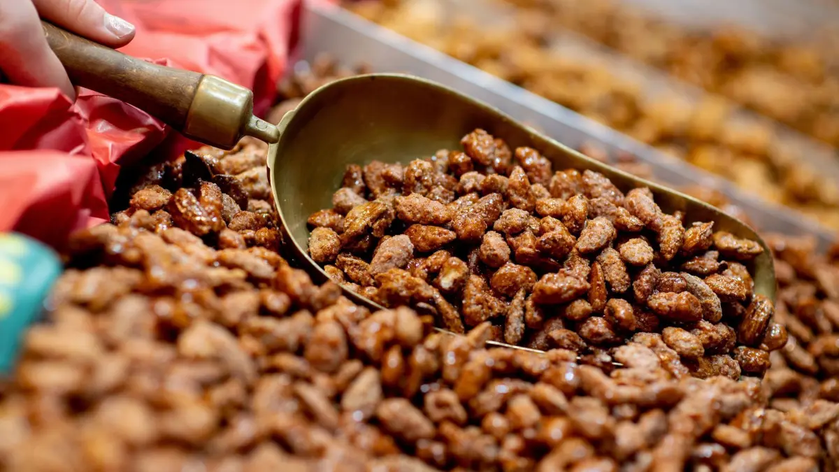 Lamberti-Markt in Oldenburg: PRODUKTION - 28.11.2024, Niedersachsen, Oldenburg: Eine Schaustellerin portioniert gebrannte Mandeln an einem Stand auf dem Lamberti-Markt. Mit rund 125 Ständen ist der Weihnachtsmarkt zwischen Rathaus und Schloss einer der größten Märkte im Nordwesten. Foto: Hauke-Christian Dittrich/dpa +++ dpa-Bildfunk +++
