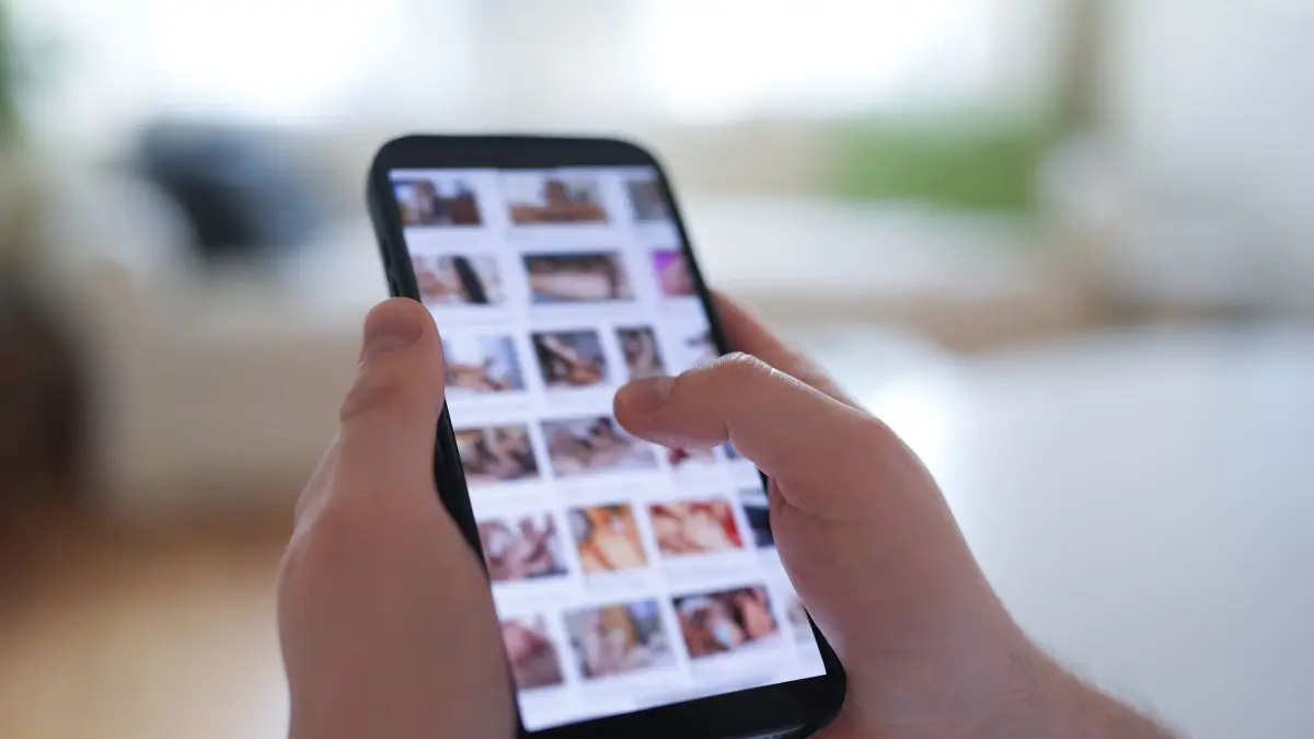 Pornografie im Internet: PRODUKTION - 14.04.2025, Hamburg: ILLUSTRATION - Ein junger Mann schaut sich auf einem Smartphone eine Porno-Internetseite an (gestellte Szene). Immer mehr Frauen und Mädchen werden Opfer von Deepfake-Pornos. (zu dpa: «Plattform für Deepfake-Pornos geht offline») Foto: Marcus Brandt/dpa +++ dpa-Bildfunk +++