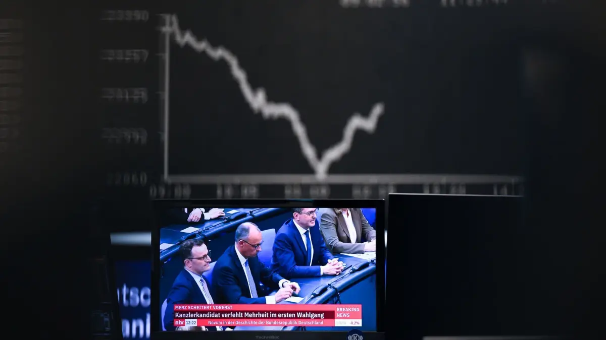 Frankfurter Börse: 06.05.2025, Hessen, Frankfurt/Main: Hinter einem TV-Monitor, auf dem der designierte Bundeskanzler Friedrich Merz (CDU, M) bei der Kanzlerwahl im Bundestag in Berlin zusehen ist, zeigt die Dax-Kurve einen fallenden Verlauf. Der designierte Bundeskanzler Merz ist bei der Kanzlerwahl im Bundestag im ersten Wahlgang durchgefallen. Foto: Arne Dedert/dpa +++ dpa-Bildfunk +++