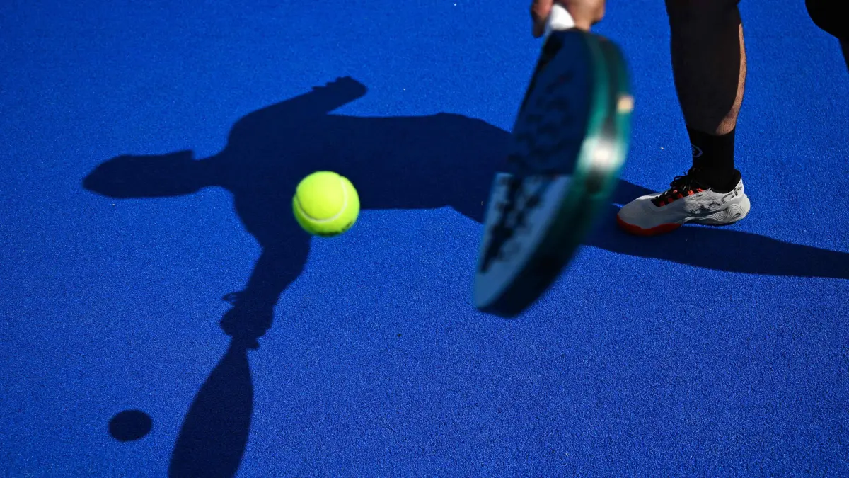 A padel tennis player is silhouetted at the Beziers Indoor Padel club in Beziers, southern France on July 22, 2025. The padel, a mixture of tennis and squash, is played in teams of two on a court that is typically surrounded by glass walls which players can bounce balls off. (Photo by GABRIEL BOUYS / AFP)