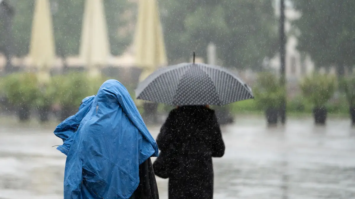 22.07.2025, Baden-Württemberg, Stuttgart: Ein Mensch schütz sich mit einer Jacke vor dem Regen, eine andere Person hat einen Schirm. (zu dpa: «Viel Regen und einzelne Gewitter zum Ende der Woche») Foto: Markus Lenhardt/dpa +++ dpa-Bildfunk +++