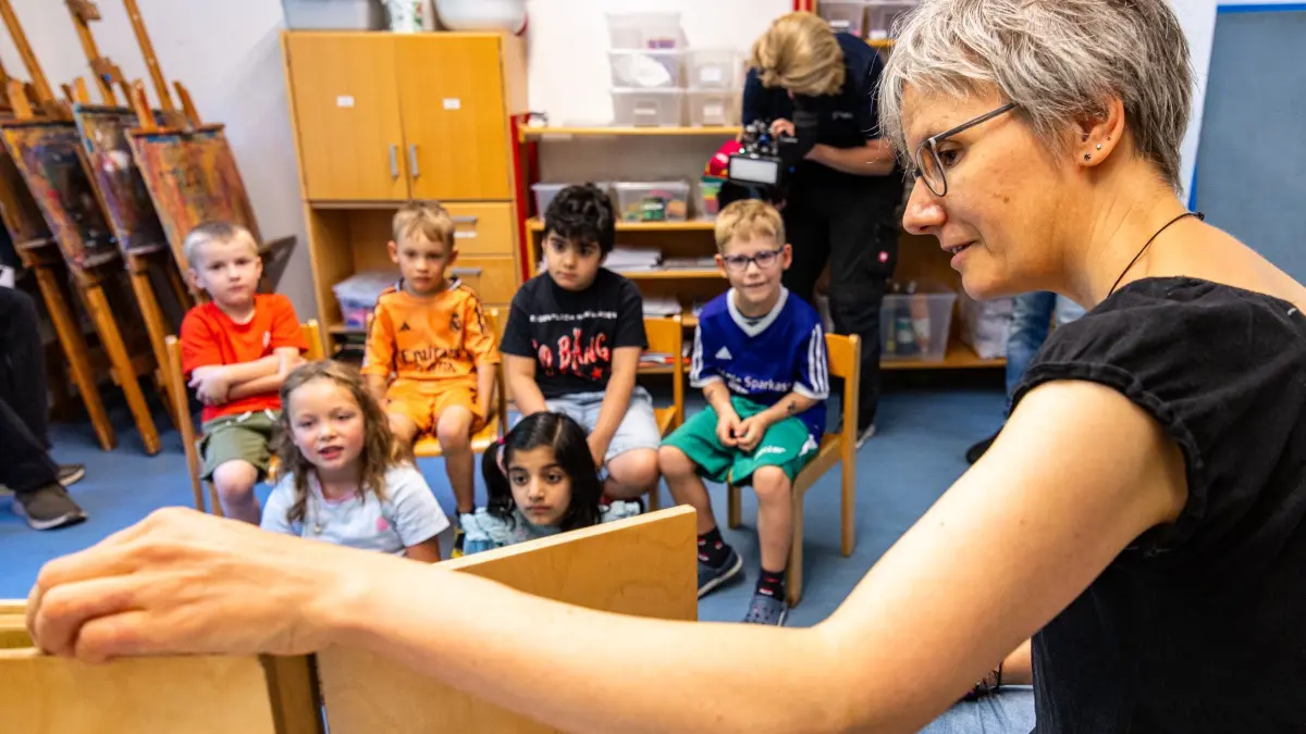 Sprachförderung in der Kita: 12.08.2025, Bremen: Sprachförderkraft Heike Willker erzählt im Kindergarten des Gemeindezentrums Martin-Luther-Findorff einer Kindergruppe eine Geschichte. Der Evangelischer Landesverband informierte in einer PK über das Kita-Jahr. Der Landesverband will mangelnde sprachliche Kompetenz thematisieren, in Bremen kann demnach fast jedes zweite Kind am Ende der Kindergartenzeit nicht ausreichend Deutsch sprechen. Foto: Markus Hibbeler/dpa - ACHTUNG: Nur zur redaktionellen Verwendung im Zusammenhang mit der aktuellen Berichterstattung und nur mit vollständiger Nennung des vorstehenden Credits +++ dpa-Bildfunk +++