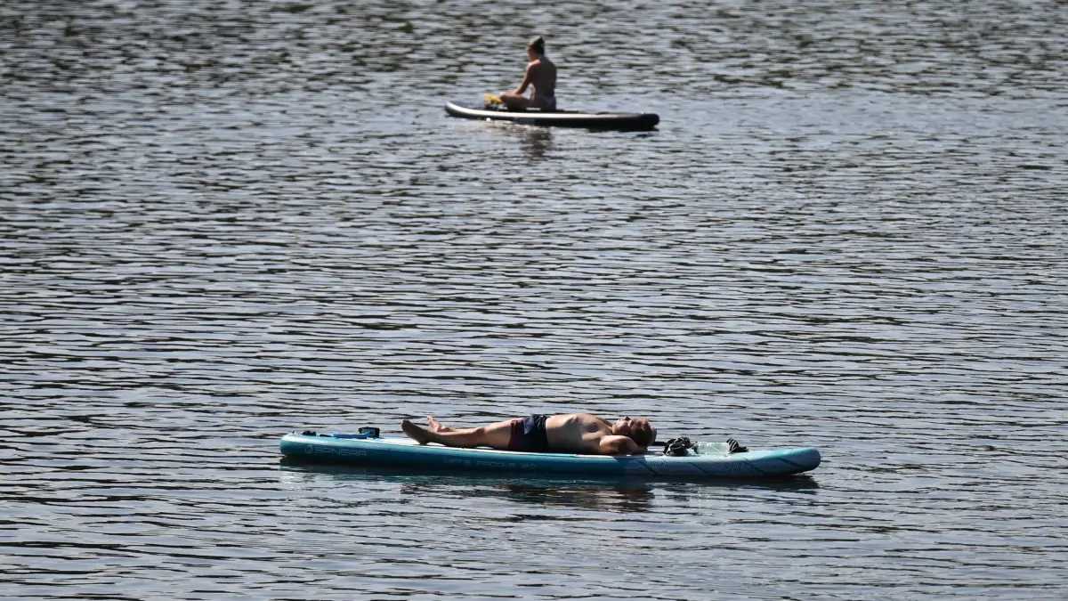 Sommerwetter - Hamburg: 13.08.2025, Hamburg: Ein Mann treibt mit seinem Stand-up-Paddle-Board (SUP) auf dem Hamburger Stadtparksee und sonnt sich. Foto: David Hammersen/dpa +++ dpa-Bildfunk +++
