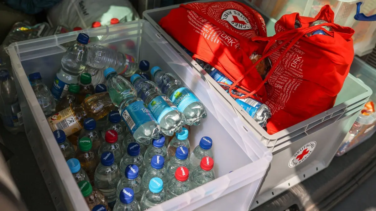 Hitzebus des DRK: PRODUKTION - 13.08.2025, Baden-Württemberg, Stuttgart: Im Hitzebus des Deutschen Roten Kreuzes (DRK) liegen in einer Kiste Wasser- und Apfelschorleflaschen bereit. Steigt das Thermometer in der Landeshauptstadt über 30 Grad, ist das orange beklebte Fahrzeug in der größten Mittagshitze unterwegs und bringt Wasser, Mützen, Sonnencreme und auch Snacks zu Obdachlosen und anderen Bedürftigen. (zu dpa: «Hilfe vom Hitzebus - «Für Wasser reicht das Geld nicht»») Foto: Christoph Schmidt/dpa +++ dpa-Bildfunk +++