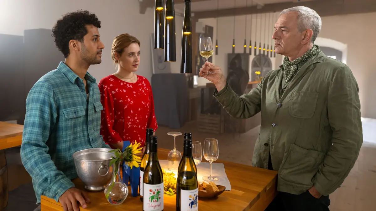 Minna (Meriel Hinsching, M.) und Lucas (Rojan Juan Barani, l.) sind gespannt, wie Zacharie Moiré (Jean-Yves Berteloot, r.) Minnas Wein mundet. Dabei hat der internationale Weinkenner große Vorurteile gegen schwedischen Wein.