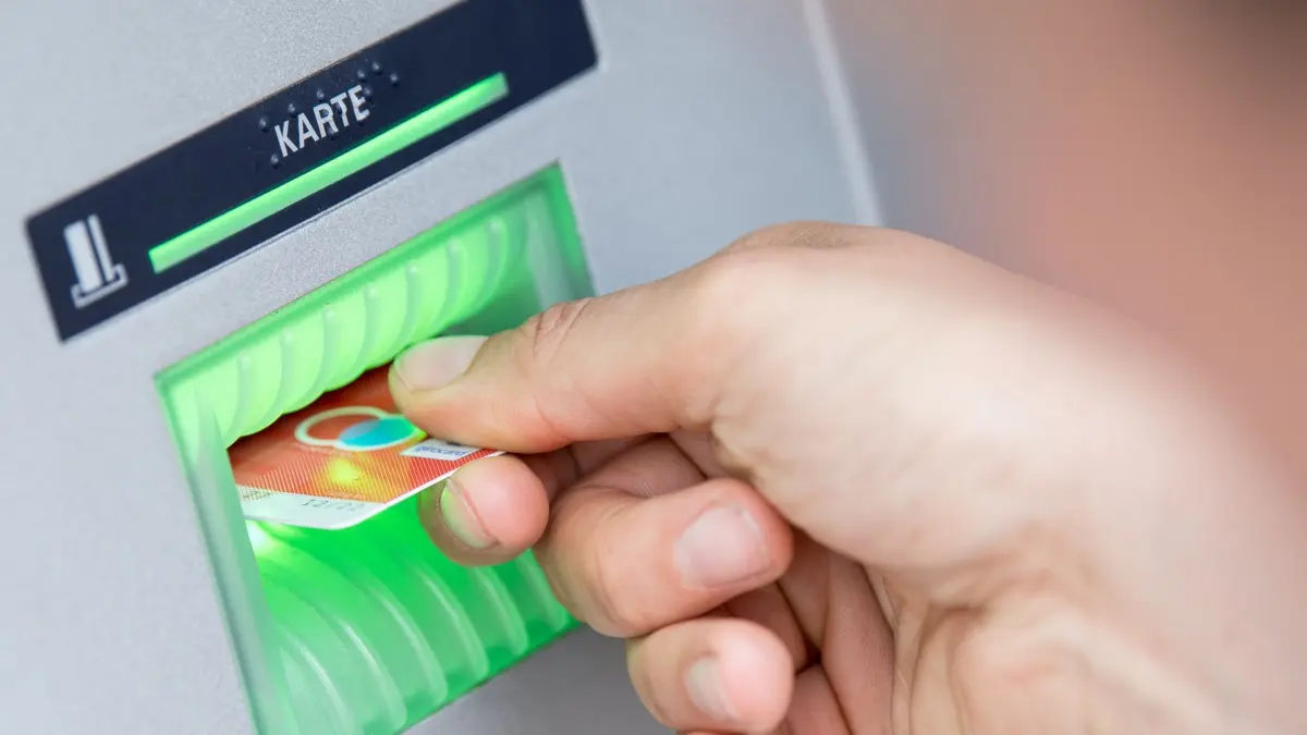 Person steckt Girokarte in einen Geldautomaten: ILLUSTRATION - Die Rentenauszahlung per Scheck wird zum Ende dieses Jahres eingestellt. Betroffene können bei Bedarf ein sogenanntes Basiskonto eröffnen. (zu dpa: «Kein Konto, keine Kohle: Rente bald nur noch per Überweisung») Foto: Fabian Sommer/dpa/dpa-tmn - Honorarfrei nur für Bezieher des dpa-Themendienstes +++ dpa-Themendienst +++