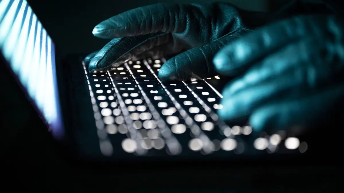 Cyberkriminalität: ILLUSTRATION - 14.12.2025, NA, Berlin: Eine Person tippt mit behandschuhten Händen auf einer beleuchteten Laptop-Tastatur. (Gestellte Szene) (zu dpa: «Jugendlicher soll Mädchen in Chat erpresst und bedroht haben») Foto: Philip Dulian/dpa +++ dpa-Bildfunk +++
