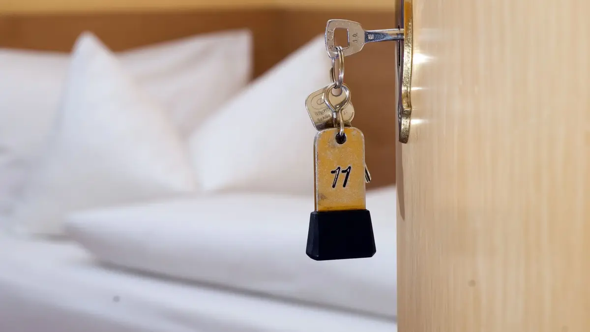Ein Zimmerschlüssel hängt in einem Gästehaus: ARCHIV - 28.11.2014, Niedersachsen, Goslar: Ein Zimmerschlüssel hängt in einem Gästehaus vor einem Bett im Türschloss. (zu dpa: «Münchner OB will mit Bettensteuer vors Verfassungsgericht») Foto: Swen Pförtner/dpa +++ dpa-Bildfunk +++