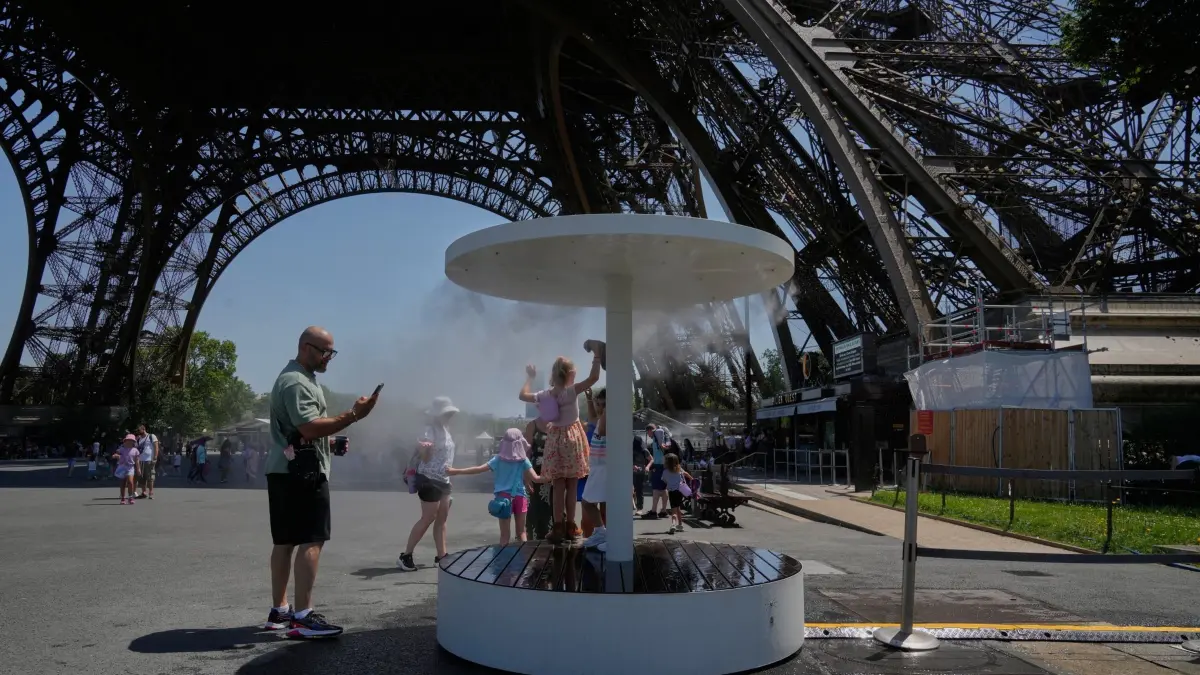 Hitze in Frankreich: 21.06.2026, Frankreich, Paris: Menschen erfrischen sich am Eiffelturm unter einem Wassersprühnebel. Foto: Michel Euler/AP/dpa +++ dpa-Bildfunk +++