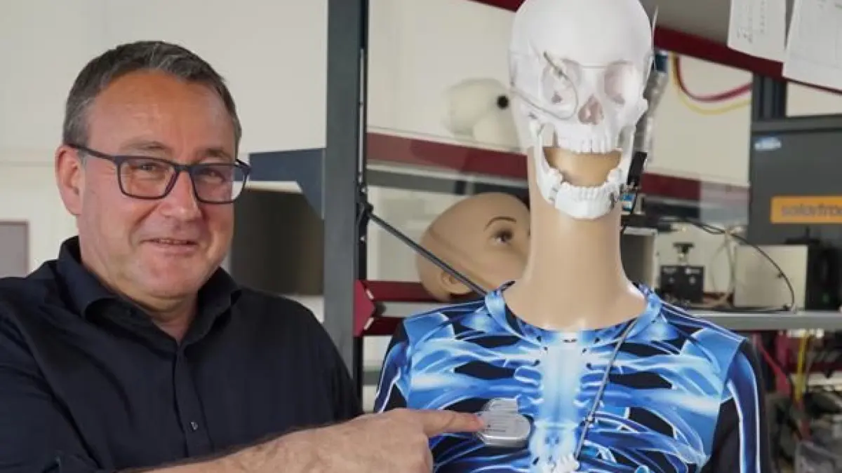 Prof. Dr. Volker Bucher neben einer Demopuppe, an der verschiedene aktive Implantate montiert sind, darunter auch Entwicklungen aus seinen Projekten – etwa ein Chip, der Blinden das Sehen ermöglicht.