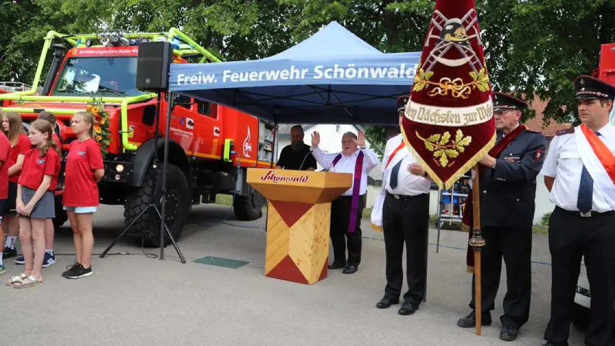 Pfarrer Andreas Treuer (Mitte) und sein evangelischer Amtskollege Arkus Ockert (links daneben) segnen die beiden Fahrzeuge. Vor dem Waldbrand-Unimog steht die Jugendfeuerwehr, rechts die Fahnenabordnung.