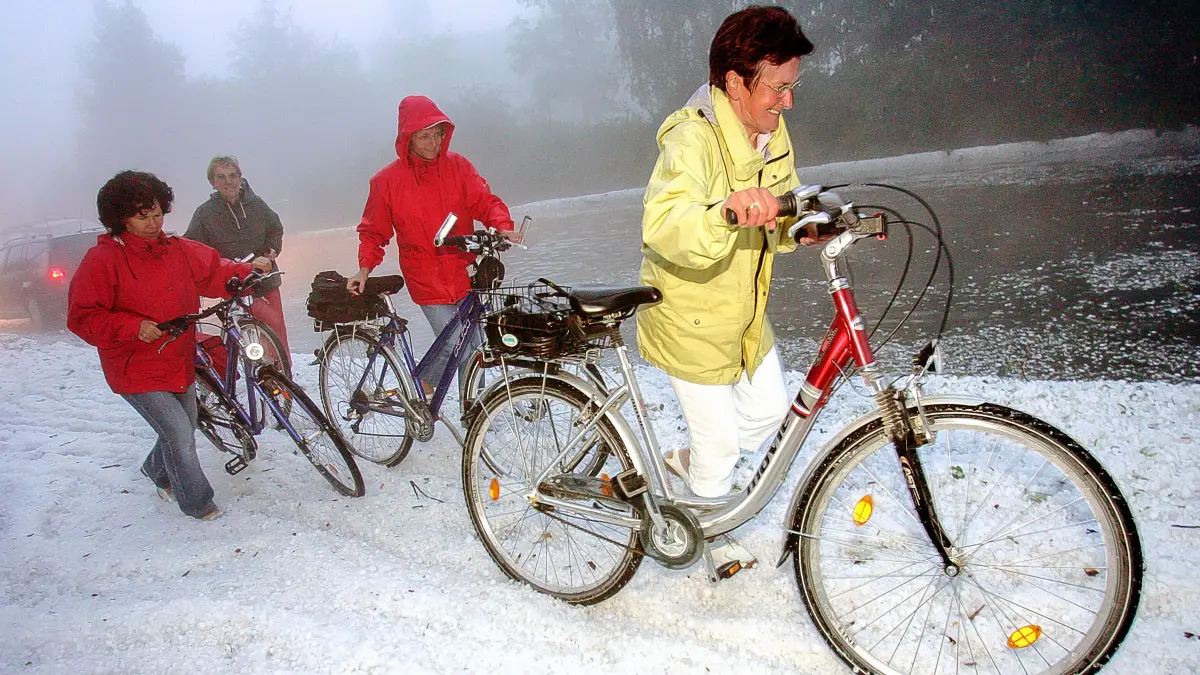 Fahrradfahrerinnen versuchen, durch die Zentimeter hohe Hagelschicht zu laufen.