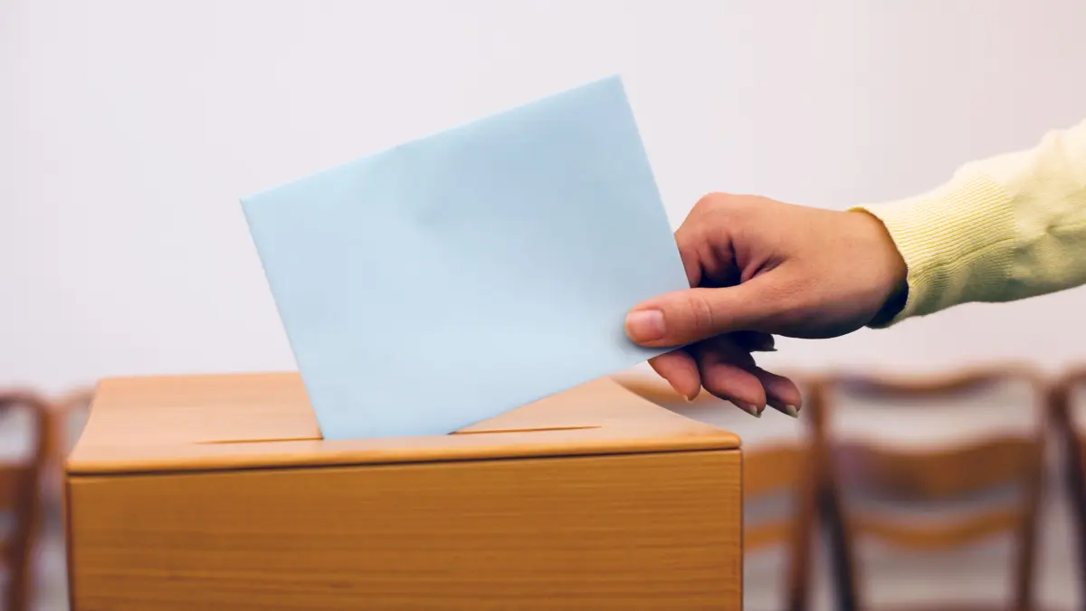 Eine junge Frau gibt bei einer Wahl ihre Wahlstimme ab. Wahlurne im Wahllokal.