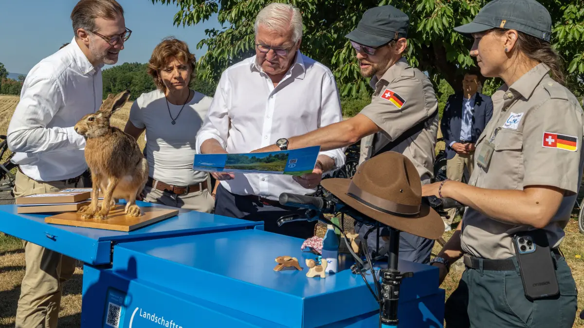 Das Ranger-Duo Martha Koelbing und Yannick Bucher informiert Bundespräsident Frank-Walter Steinmeier über die besonderen Herausforderungen im Landschaftspark Wiese. Auch der Basler Regierungspräsident Conradin Cramer und die Riehener Gemeindepräsidentin Christine Kaufmann hören interessiert zu.