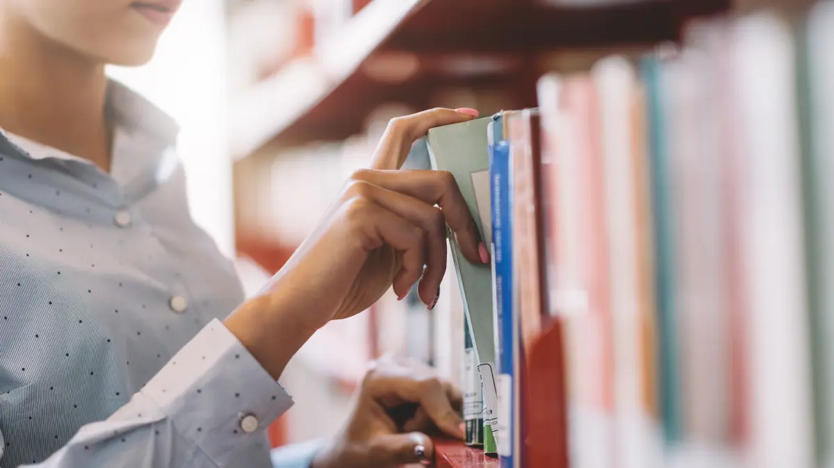 Woman at the library, she is searching books on the bookshelf and taking a textbook on the shelf, hand close up