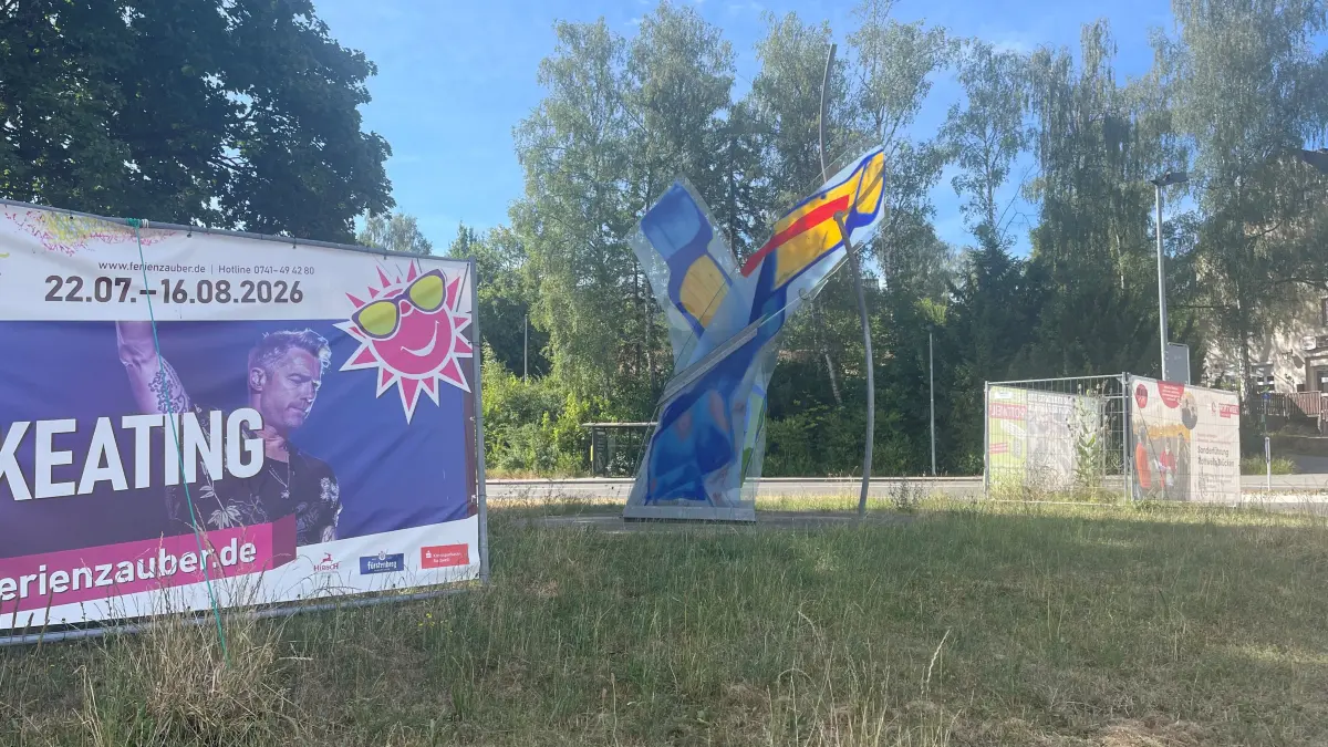 Die Glasskulptur "Potenzial des Aufbruchs" von Tobias Kammerer wird von zwei Bauzäunen mit Werbeplakaten eingefasst. Schön ist anders.
