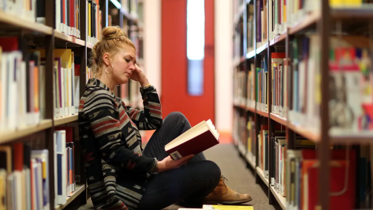 ILLUSTRATION - Eine Frau sitzt am 13.12.2018 in der Bibliothek der Universitaet Oldenburg (Niedersachsen) vor einem Buecherregal und liest etwas (gestellte Szene). Foto: Markus Hibbeler || Modellfreigabe vorhanden