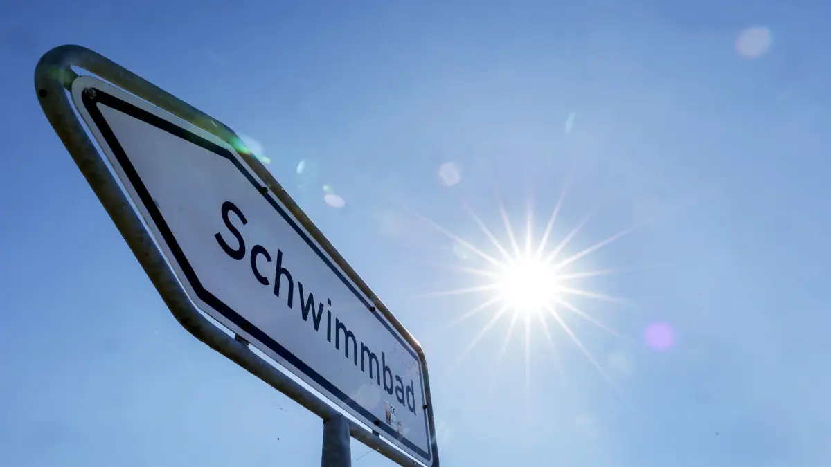 Wetter in Baden-Württemberg: 12.07.2026, Baden-Württemberg, Uttenweiler: Die Sonne strahlt über einem Wegweiser mit der Aufschrift "Schwimmbad". Für den Tag sind Temperaturen über 30 Grad vorhergesagt. Foto: Thomas Warnack/dpa +++ dpa-Bildfunk +++