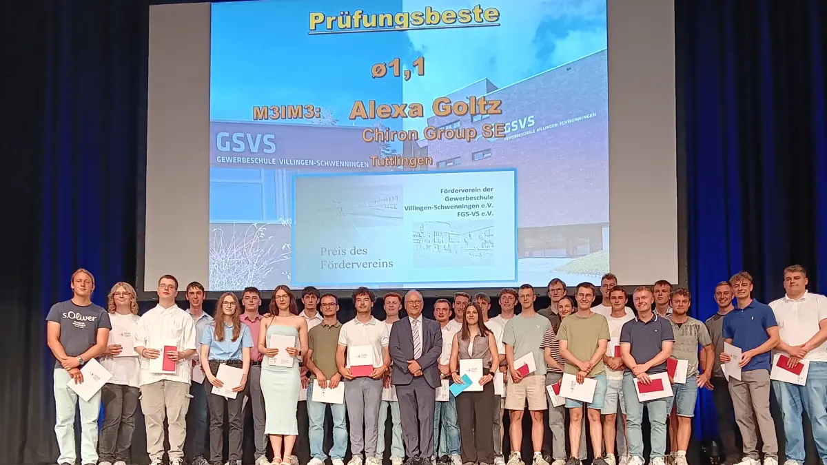Die Prüfungsbeste Alexa Goltz (blaues Kuvert in der Hand) steht neben Schulleiter Svjetlan Magazinović auf der Bühne der Neckarhalle und freut sich mit den anderen für ihre Leistungen mit einem Preis ausgezeichneten Berufsschulabsolventen der Gewerbeschule in der Neckarhalle über den Applaus. Die Preisträger von links nach rechts: Jannick Behringer, Mary Schneider, Maximilian Krech, Nieklas Hiemer, Natalia Krey, Samuel Kurz, Sabrina Träger, Frederik Faller, David Kammerer, Erwin Haas, Thilo Gauß, Schulleiter Magazinović, Jannik Meßmer, Timo Klausmann, Alexa Goltz, Julian Lauble, Sebastian Fritz, Lasse Schneider, Vanessa Gut, Felix Reichart, Valentin Schmidt, Simon Pfaff, Alexander Riesle, Noah Geißler, Paul Schmid, Thorben Hogg, Maximilian Herr, Cyrill Bossauer (Foto: GSVS) eilen
