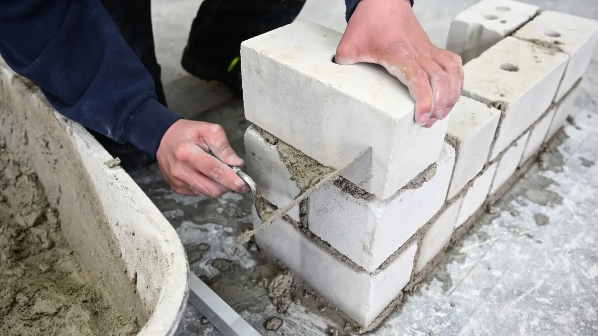 Ausbildung: ARCHIV - 14.03.2019, Baden-Württemberg, Ravensburg: Ein Auszubildender im Maurer-Handwerk nimmt in einem Ausbildungszentrum mit der Kelle den überstehenden Mörtel von der Mauer, die er im Unterricht gebaut hat. (zu dpa: «EU vermutet Preisabsprachen bei Bauchemie-Herstellern») Foto: Felix Kästle/dpa +++ dpa-Bildfunk +++