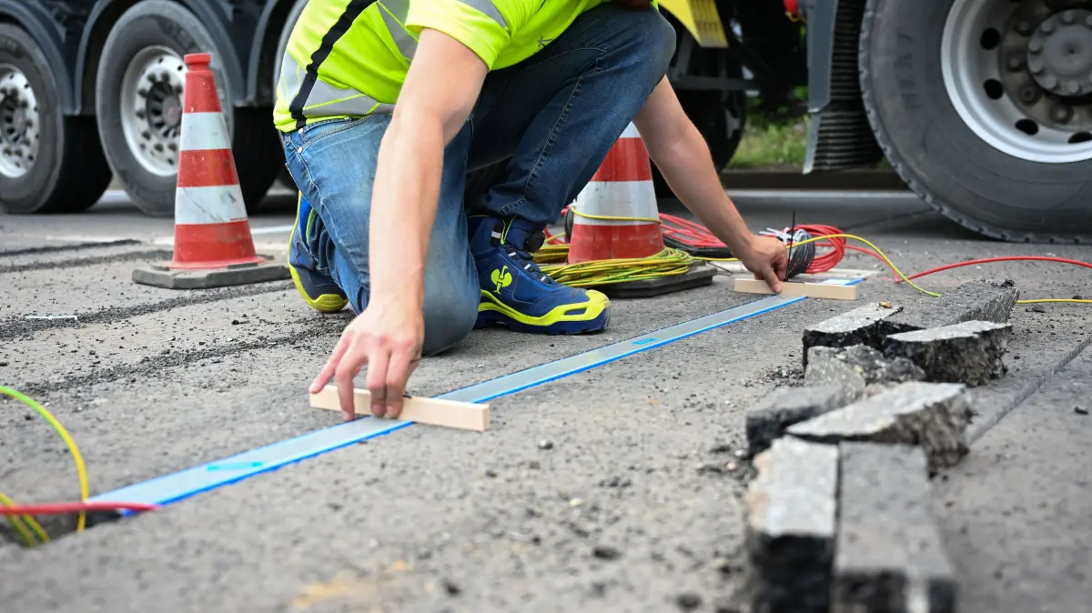 15.07.2026, Sachsen, Dresden: Ein Servicetechniker setzt einen Messbalken auf einer Baustelle zum Einbau von Achslast- und Temperatursensoren in Dresden in dafür vorgesehenes Loch während ein Lastwagen vorbeifährt.
Die mithilfe der Sensoren erfassten Daten sollen helfen, den Zustand der Straßen besser zu bewerten und künftige Straßenbaumaßnahmen effektiv zu planen. Foto: Katharina Kausche/dpa +++ dpa-Bildfunk +++
