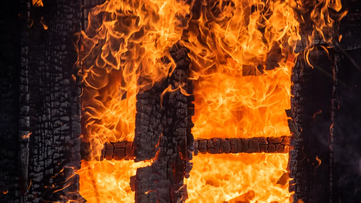 Dangerous fire. Whole house and yard on fire. A fire destroys a charred burnt house. Charred in flame house at night. Fire everywhere and smoke in a residential area at night