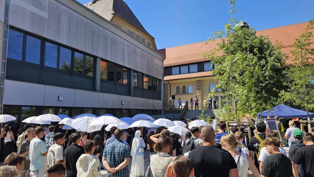 Optisch wirkungsvoll inszenierten Schüler eine kleine Demo auf dem Schulhof mit weißen Schirmen, um auf den fehlenden Sonnenschutz des Campus' hinzuweisen.