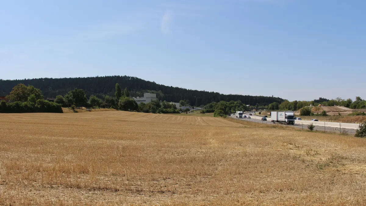 Direkt an der A81 soll eine landwirtschaftliche Nutzfläche mittels Agri-PV-Anlage zusätzlich zur Stromerzeugung genutzt werden. Im Hintergrund liegen von links nach rechts die Schuppenkolonie „Auf Stauden“ (hinter den Bäumen), das stillgelegte Gipswerk, das Gewerbegebiet Wörth sowie die Baustelle für den Lärmschutzwall (ganz rechts).