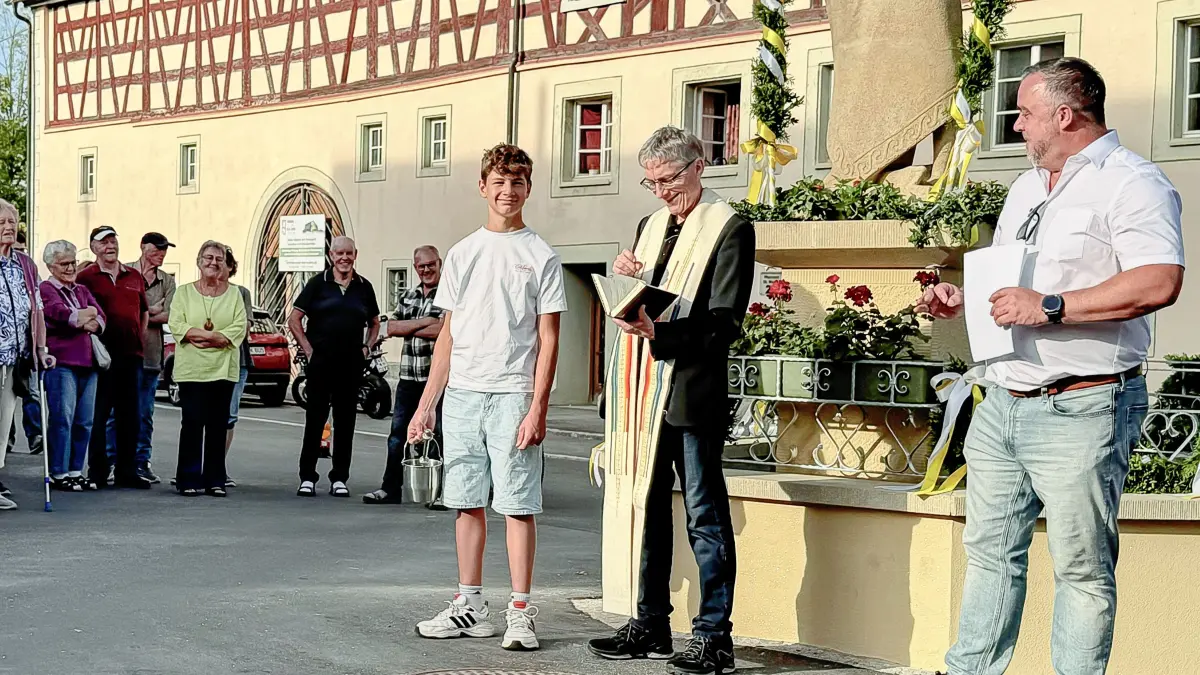 Ministrant Elias Schey, Pfarrer Karlheinz Brandl und Bürgermeister Markus Keller vor 150 Teilnehmern der Brunnenweihe.