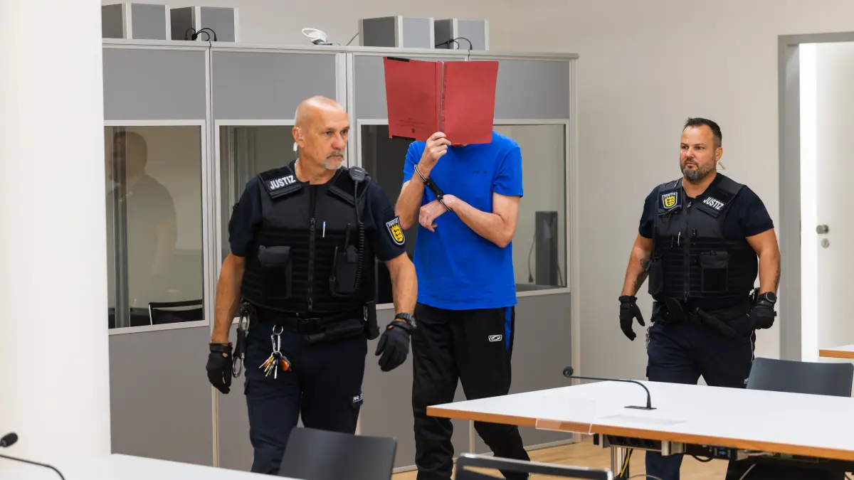 01.07.2026, Baden-Württemberg, Freiburg: Ein Angeklagter (M) wird von Justizbeamten in den Verhandlungssaal geführt. Der 58-jährige Angeklagte soll im Oktober 2025 in Bollschweil (Landkreis Breisgau-Hochschwarzwald) seine achtjährige Tochter getötet haben. Das Verfahren wurde von einem Sicherungs- in ein Strafverfahren überführt, nachdem ein zweites vorläufiges psychiatrisches Gutachten zu dem Ergebnis kam, dass der Angeklagte nicht in seiner Schuldfähigkeit eingeschränkt gewesen sein soll. Foto: Philipp von Ditfurth/dpa +++ dpa-Bildfunk +++