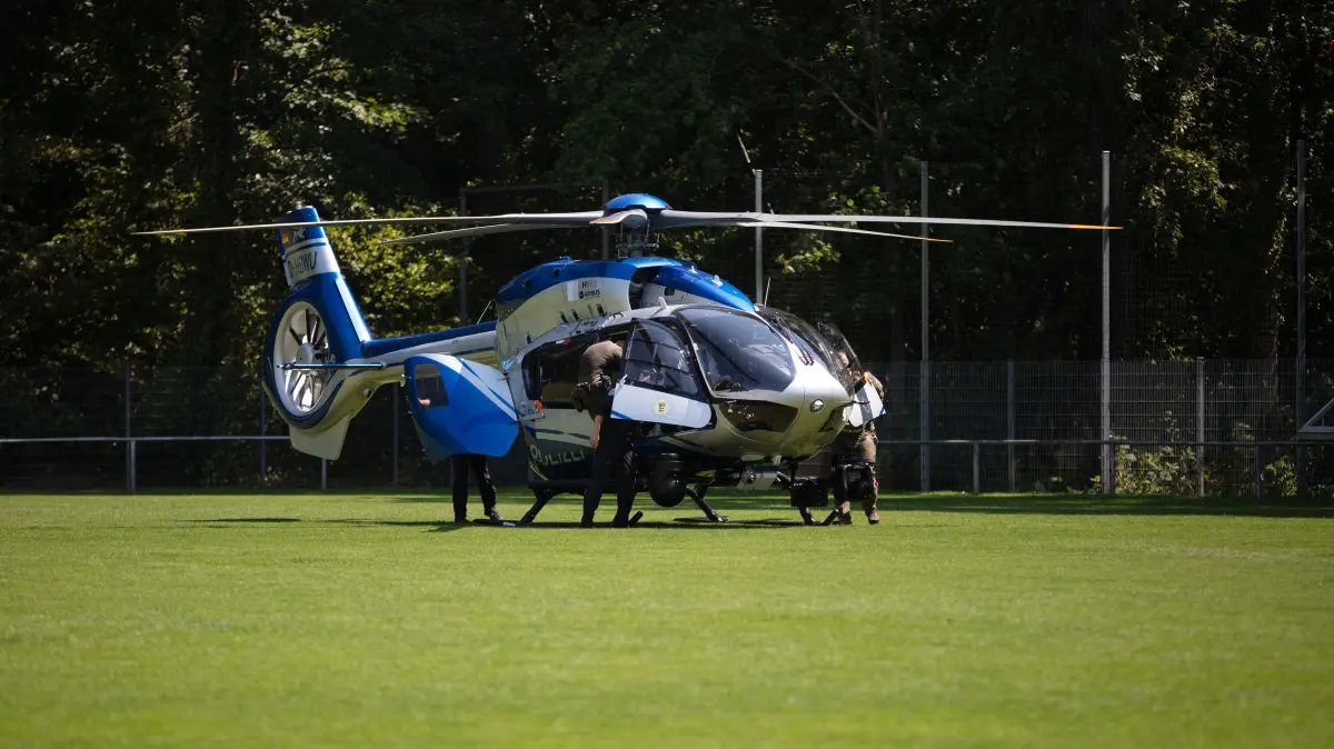 Polizisten stehen in Weil am Rhein an einem Polizeihubschrauber, der zuvor auf einem Fußballplatz gelandet war.