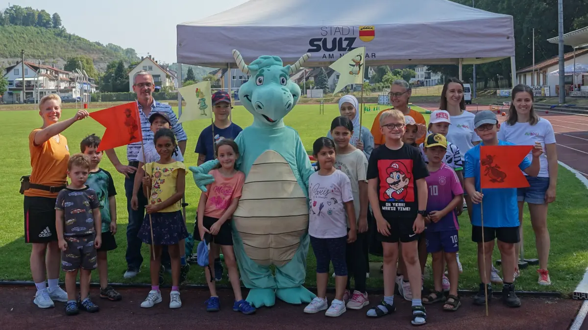 Am Beginn der Sommerferien strahlen sie mit der Sonne um die Wette: Salzdrache Streusel, viele sportbegeisterte Kinder, Bürgermeister Jens Keucher und das Team von „Spiel und Spaß im Albeck-Stadion“.