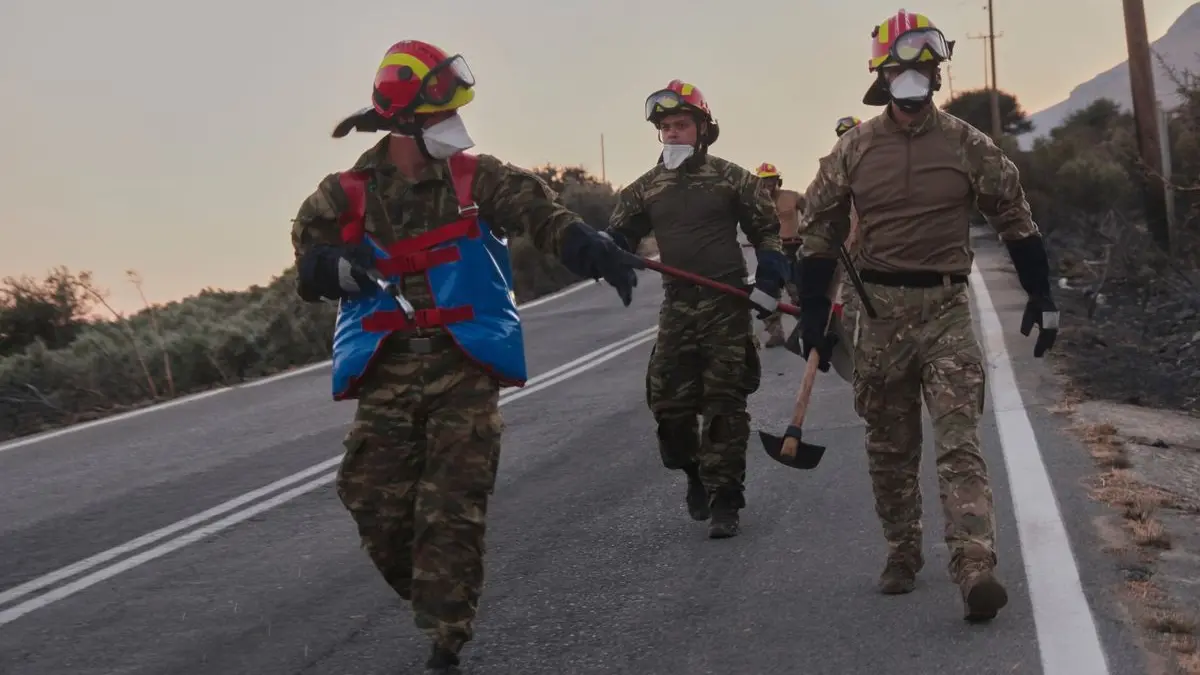 Feuerwehrleute gehen während eines Waldbrands in der Region Rethymno auf der südgriechischen Insel Kreta mit Werkzeugen eine Straße entlang.