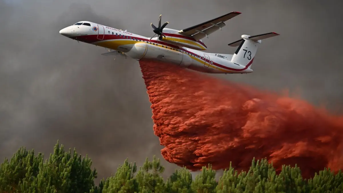 Eine De Havilland Canada Dash 8-400 versprüht Löschmittel, während sie über einen Wald fliegt.