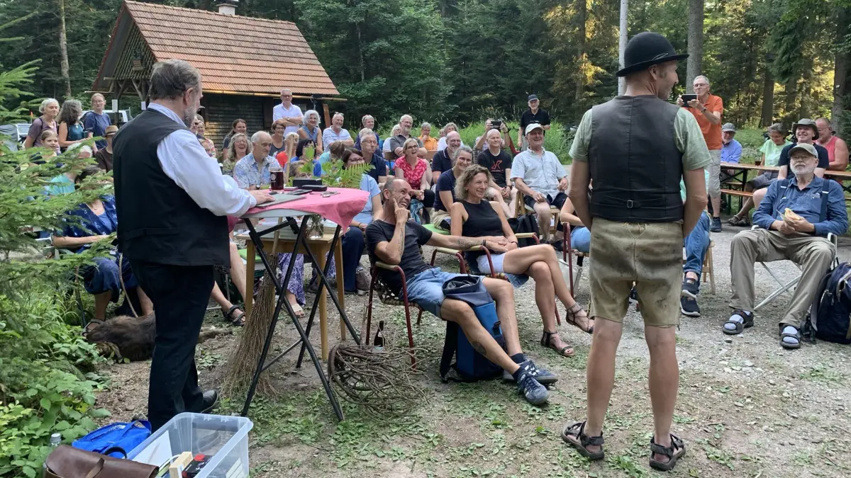 Dichterlesung unter alten Bäumen. Ein stimmungsvolles Bild an einem stimmungsvollen Platz gaben die Zuhörer bei der Krimilesung an der Hausserhütte im Stadtwald im ab. Über seine Arbeit als Köhler informiert Thomas Faißt (rechts).