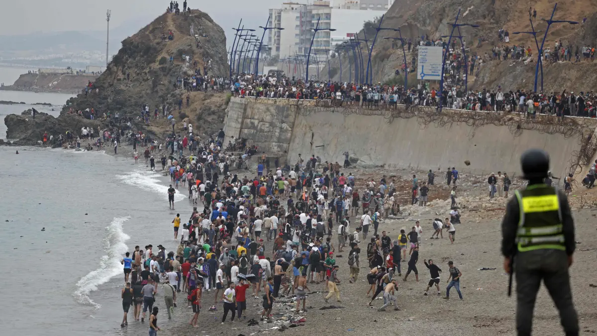 MOROCCO-SPAIN-MIGRATION: People gather along the fence at the site of clashes near Fnideq, on the Morocco-Spain border, on July 31, 2026. Thousands of migrants crossed overnight from Morocco into Spain's north Africa's Ceuta enclave, a police source said on July 31, adding that it was impossible to estimate how many people in total. A total of 18 people died while attempting to reach the Spanish enclave, the source said. (Photo by Abdel Majid BZIOUAT / AFP)