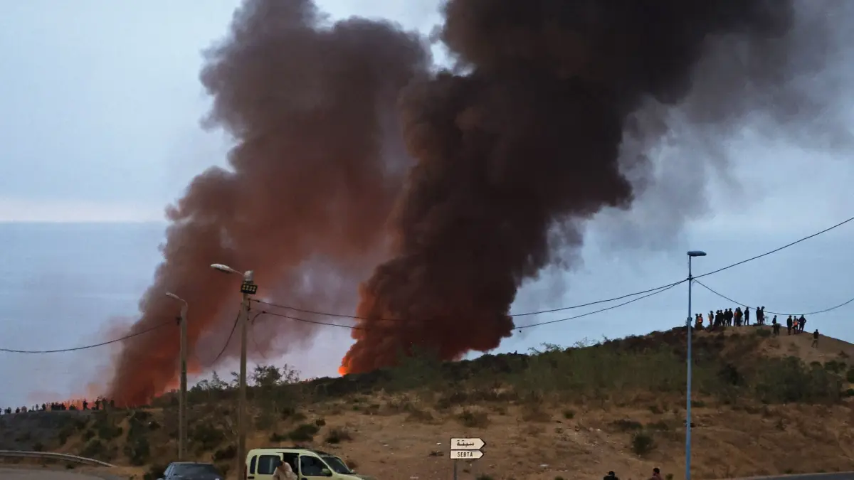 MOROCCO-SPAIN-MIGRATION: Smoke billows from the site of clashes near Fnideq, on the Morocco-Spain border, on July 31, 2026. Thousands of migrants crossed overnight from Morocco into Spain's north Africa's Ceuta enclave, a police source said on July 31, adding that it was impossible to estimate how many people in total. A total of 18 people died while attempting to reach the Spanish enclave, the source said. (Photo by Abdel Majid BZIOUAT / AFP)