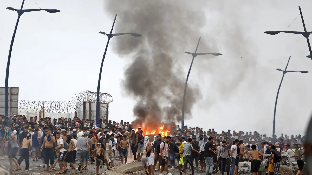 MOROCCO-SPAIN-MIGRATION: People gather at the site of clashes near Fnideq, on the Morocco-Spain border, on July 31, 2026. Thousands of migrants crossed overnight from Morocco into Spain's north Africa's Ceuta enclave, a police source said on July 31, adding that it was impossible to estimate how many people in total. A total of 18 people died while attempting to reach the Spanish enclave, the source said. (Photo by Abdel Majid BZIOUAT / AFP)