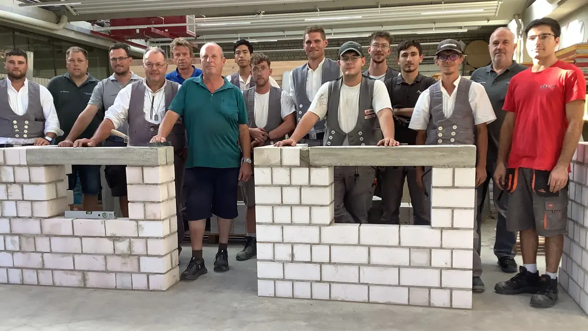 Die Junggesellen und der Gesellenprüfungsausschuss der Innungen Calw/Nagold und der Bauinnung Freudenstadt hinter den Gesellenstücken, einer gemauerten Wandecke mit Fensteröffnung