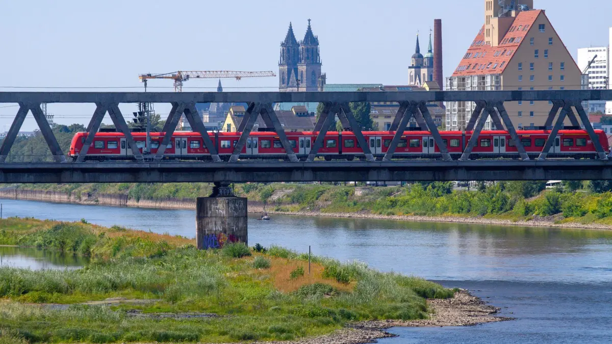 Niedrigwasser an der Elbe: 03.08.2026, Sachsen-Anhalt, Magdeburg: Ein Zug fährt an der Mündung der Alten Elbe über eine Elbe-Brücke. Der Wasserstand am Elbe-Pegel Magdeburg-Strombrücke ist weiter auf einem sehr niedrigen Niveau. Abschätzungen zufolge kann der Wasserstand am 06. August 2026 abends 42 Zentimeter betragen, einen Tag später sogar 40 Zentimeter betragen. Foto: Klaus-Dietmar Gabbert/dpa +++ dpa-Bildfunk +++