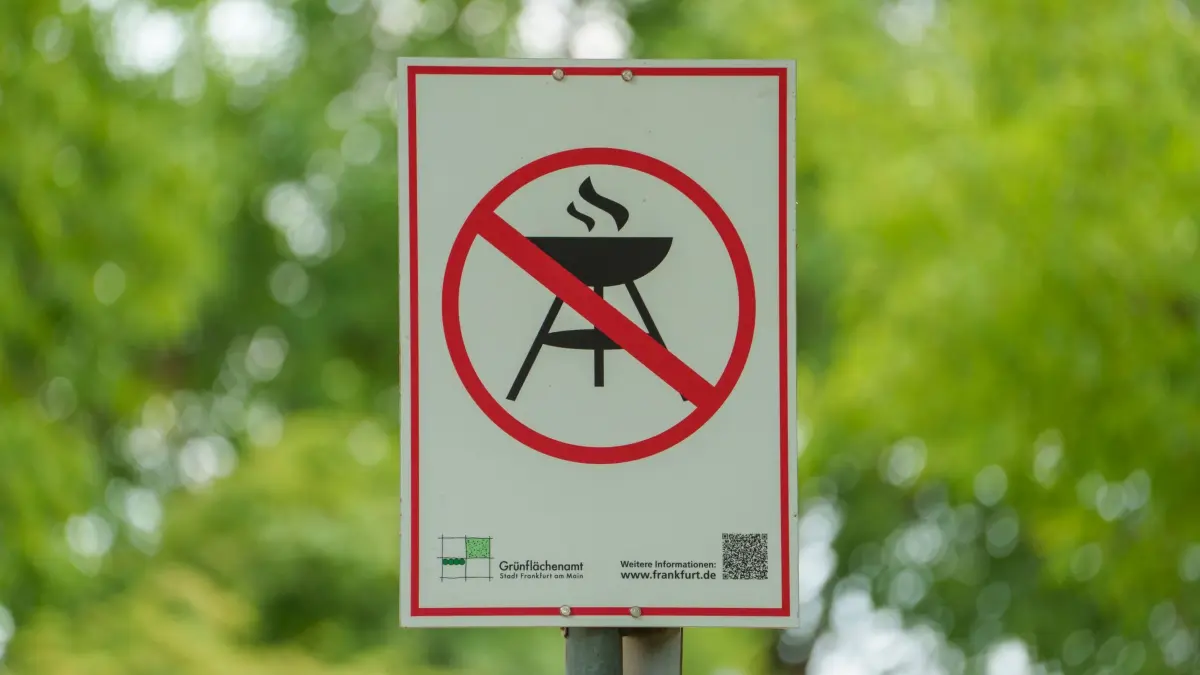 Grillen in öffentlichen Parks: ARCHIV - 08.07.2025, Hessen, Frankfurt/Main: Ein Schild auf dem Lohrberg weist mit einem Piktogramm auf das Grillverbot hin. Am Mittwoch, dem 9. Juli, tritt in Frankfurt ein umfassendes Grillverbot in städtischen Grünanlagen in Kraft. Die Entscheidung des Umweltdezernats erfolgt auf Grundlage der anhaltend trockenen Witterungsverhältnisse – trotz gelegentlicher Regenschauer bleibt die Lage angespannt. (zu dpa: «Waldbrandgefahr: «Nicht rauchen, nicht grillen, nur chillen»») Foto: Andreas Arnold/dpa +++ dpa-Bildfunk +++