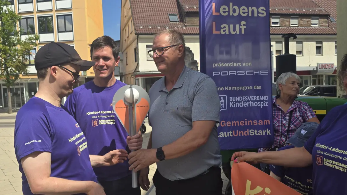 Oberbürgermeister Jürgen Roth übergibt die Fackel an Maximilian Kolk von der Mobilen Kinderkrankenpflege. Deren Geschäftsführer Sebastian Pietsch ist auch mit dabei und unterstützt die Aktion.