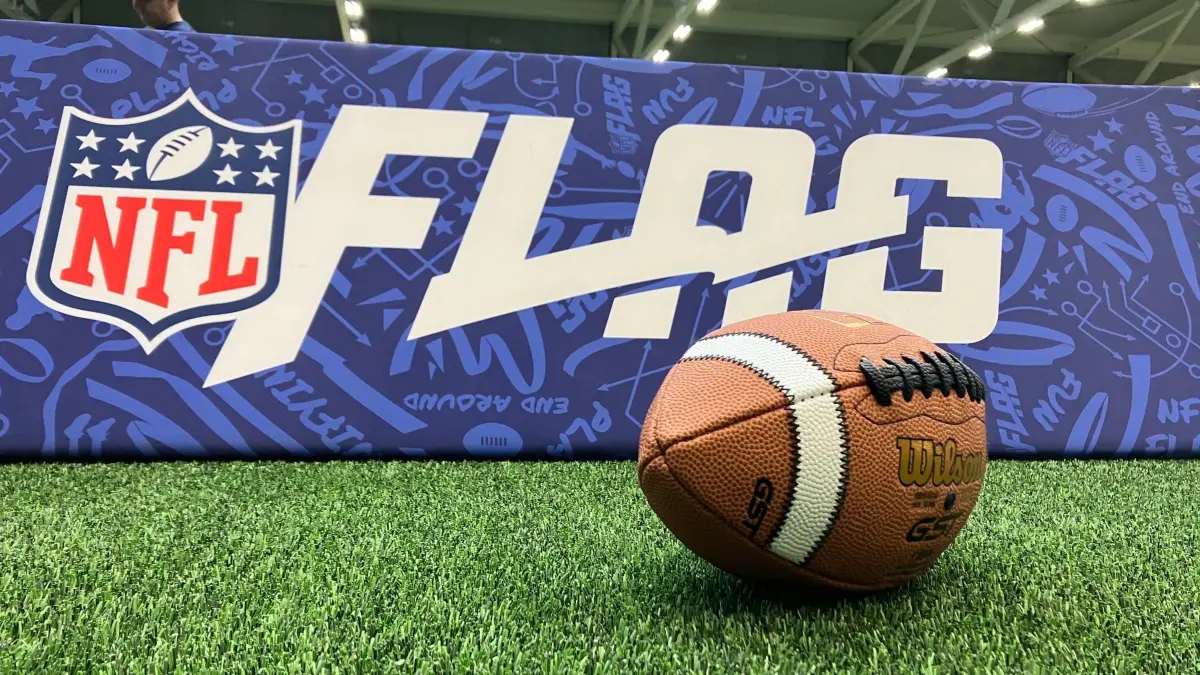 Flag Football: ARCHIV - 09.11.2023, Hessen, Frankfurt/Main: Ein Football liegt bei einem Presseevent vor einer Werbebande mit der Aufschrift "Flag" mit dem Logo der NFL. Flag Football wird 2028 olympisch. (zu dpa: «Auf dem Weg zu Olympia: Flag-Football-WM in Düsseldorf») Foto: Alina Grünky/dpa +++ dpa-Bildfunk +++