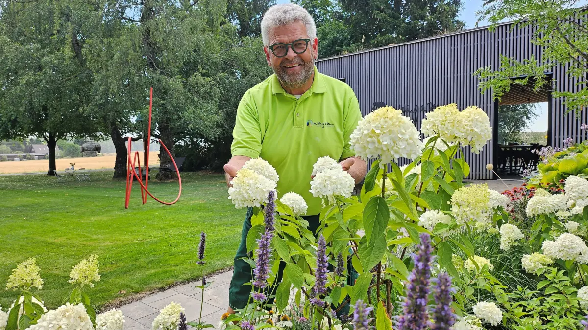 Dietmar Wildi in seinem Privatgarten: Bäume beschatten den Rasen. Drumherum blüht es in vielen Farben.
