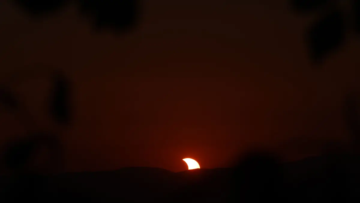 Die Sonne, die aussieht wie der Mond, geht hinter einem Berg unter.