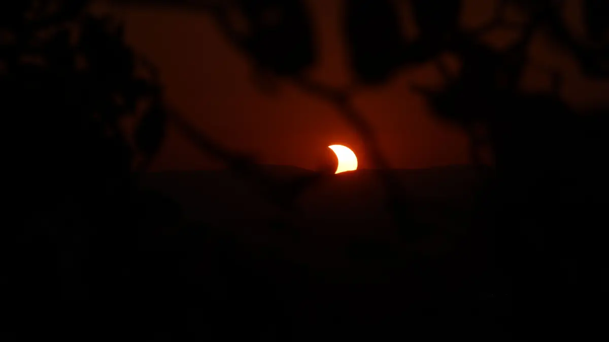 Die Sonne, die aussieht wie ein Mond geht hinter einem Berg unter.